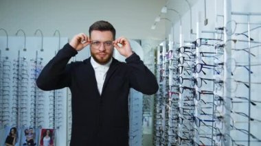 Optik mağazasında gözlük seçen bir adam. Genç çekici adam yeni gözlükleri test ediyor.