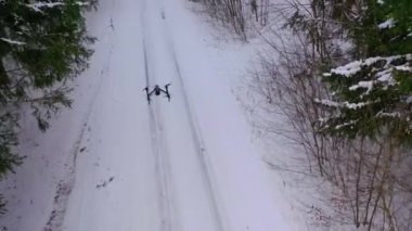Karla kaplı bir dron ormanın üzerinde uçuyor. Uçan İHA kış kar manzarası arka planında faaliyet gösteriyor