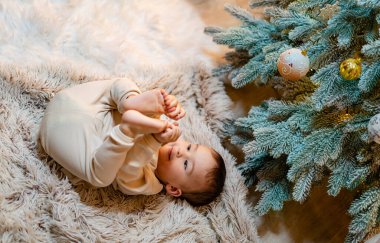 Halıya uzanmış bir bebek, noel ağacının yanında. Halıda yatan bir bebek Noel ağacının yanında