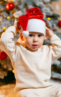 Noel ağacının önünde oturan küçük bir çocuk. Noel 'in Büyüsüne kapılmış Küçük Çocuk