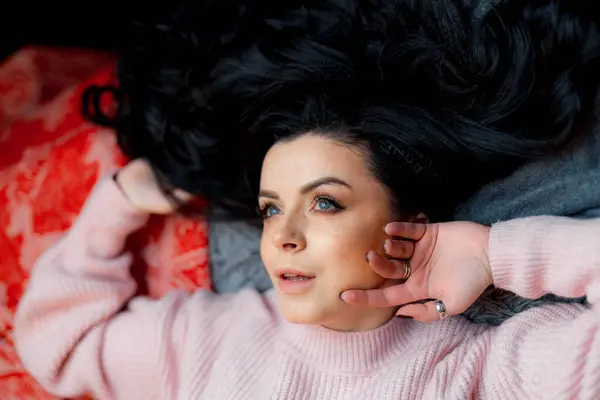 A woman laying on top of a bed in a pink sweater. A Woman Laying on Top of a Bed in a Pink Sweater