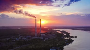 Önünde elektrik santrali olan güzel bir gün batımı. Nehrin yukarısında kırmızı ve sarı gökyüzü. İnsansız hava aracından video.