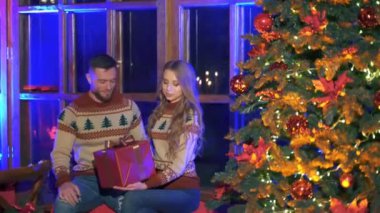 Mutlu romantik çift Noel 'i ya da yeni yılı birlikte kutluyorlar. Kadın hediye alıyor. Erkek ve dişi Noel ağacının yanında oturuyor..