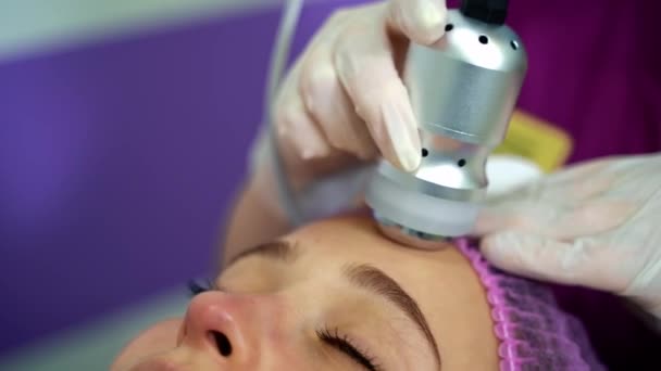 美しい女性は治療を持ち上げています 美容院で顔の肌をきつく締める手順を受けている魅力的な少女 ハードウェアスキントリートメントを行うプロの化粧品学者 — ストック動画