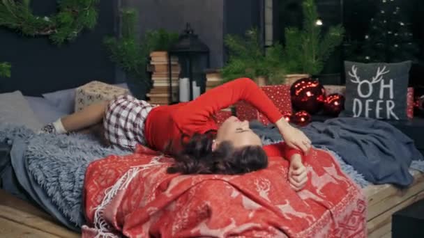 とても美しい女の子がベッドに転がり カメラに向かってポーズをとります 冬の休日の前の部屋のインテリア フェストスピリット — ストック動画