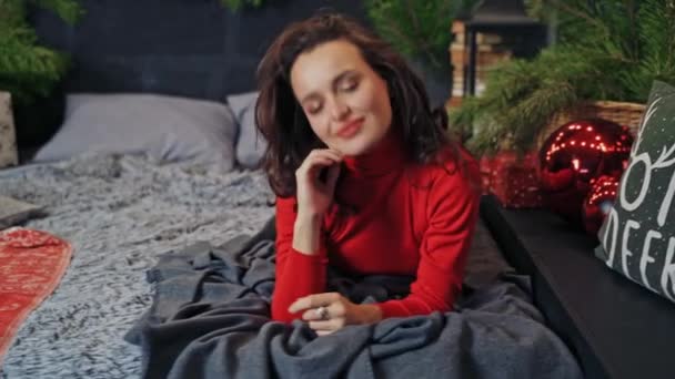 かわいいブルネットは冬の休暇の前にベッドに横たわってポーズをとっています 幸せな女性は祭りの時を待っています — ストック動画