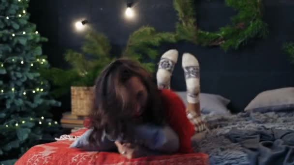 幸せで元気な女性がベッドの枕で倒れています 冬休み前に装飾されたインテリア — ストック動画