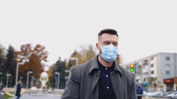 若いビジネスマンは 強い表情とフェイシャルマスクで屋外をポーズしています ストリートを歩く灰色のコートとダークスーツの男性 コンセプト ビデオ — ストック動画