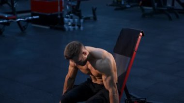 Mükemmel vücutlu vücut geliştirici ve dambılı güçlü eller. Modern spor salonunun karanlık arka planı. Yavaş çekim.