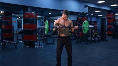 Güçlü vücudu ve çıplak gövdesi olan erkek sporcu modern spor salonunda halter kaldırıyor. Yavaş çekim.