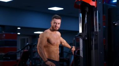 Vücut geliştirici poz veriyor. Güzel sporcu erkek gücü. Fitness, koyu renk jimnastik geçmişi olan tişörtsüz kaslı bir adam. Yavaş çekim.