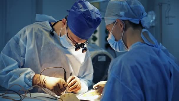 전문가들은 병원에서 수술을 있습니다 머리에 확대경을 외과의사는 수술실에서 보조원들 일하고 — 비디오