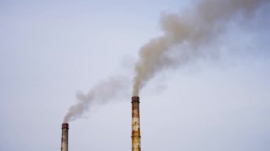 Endüstriyel santrallerin yüksek bacaları gökyüzü arka planında sigara içerler. Kirli fabrika bacaları havaya büyük dumanlar üflüyor. Kimya endüstrisi tarafından çevresel zehirlenme.