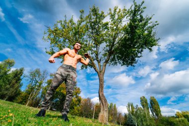 Tişörtsüz Adam Ağacın Yanında Güçlü Poz Veriyor. Bir ağacın yanında üstsüz bir adam duruyor.