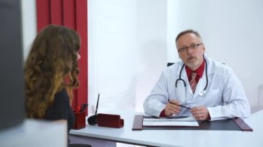 Klinikte danışmanlık yapan genç bayan hastaya yan bakış. Beyaz üniformalı, orta yaşlı, olgun bir erkek doktor. Sağlık hizmeti kavramı.