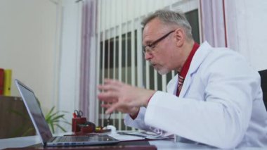 Modern klinikte dizüstü bilgisayarda çalışan mutlu bir doktor. Online danışmanlık. Klinikte uzman bir doktor hastayla internette konuşuyor..