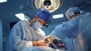 Deneyimli sağlık görevlileri, nörocerrahları modern klinik odasında parlak ışıkla zor bir operasyon sağlıyorlar..