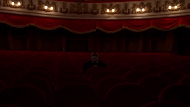 男は赤い劇場の椅子から立ち上がり 医療用マスクを捨てた 空いているホールの訪問者 パンデミックコンセプトを停止 — ストック動画