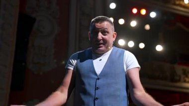 Takım elbiseli bir adam sahnede mikrofonda şakalar yapıyor. Komik performans. İyi mizah anlayışı olan bir komedyen seyirciye konuşur..