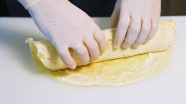 Et ve peynirli shawarma pişiriyorum. Lateks eldivenli eller pide rulosunu sarar. Yakın plan..