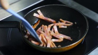 Şef kahvaltı hazırlıyor. Yağlı ve renkli harika bir domuz pastırması yapmak. Sıcak bir tavada cızırdıyor ve sigara içiyor.