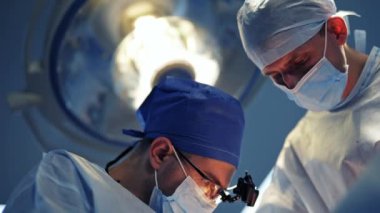 Modern ekipmanlarla klinikte operasyon. Mikroskopla ameliyat. Tıbbi maskeli ve üniformalı doktorlar. Süreçle ekranlar.