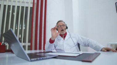 Modern klinikte dizüstü bilgisayarda çalışan mutlu bir doktor. Online danışmanlık. Klinikte uzman bir doktor hastayla internette konuşuyor..