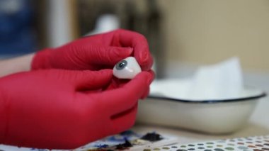 Oftalmolog plastik gözü elinde tutuyor. Detaylı göz modeli. Kırmızı lateks eldivenli ellere odaklan.
