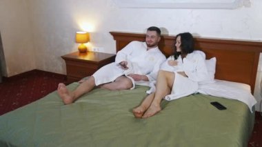 Bornozlu mutlu çift otel odasının arka planında. İnsanlar, seyahat, turizm, tatil ve balayı konsepti.