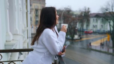 Kar beyazı bir bornozla balkonda sabah bir fincan çayla güzel bir genç kız. Evden uzakta iyi tatiller. Oteldeki kadın..