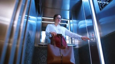 Yeni iş seyahatine hazırım. Kendine güveni tam genç iş kadını asansörde bavulla dikilirken düğmeye basıyor..