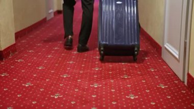 Otelde kalırken koridor boyunca hareket eden bavullu zarif iş adamının arka görüntüsü..