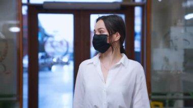 Koronavirüsten korumak için koruyucu maske takan sevimli genç bir bayan otel konuğu. Beyaz gömlekli bir kız otele girer..