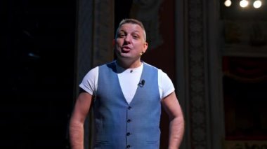 Showman, seyirciyi ışık altında eğlendirir. Büyük sahne. Sahneden ciddi bir sanatçı konuşuyor. Eller cepte..