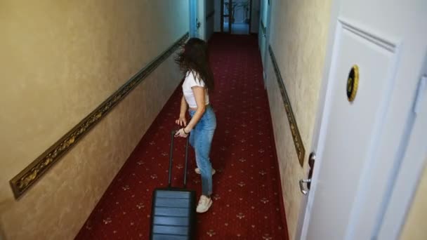 女人拿着手提箱在酒店走廊 可爱的快乐的女孩搬进了一家旅馆 正在寻找她的房间 — 图库视频影像