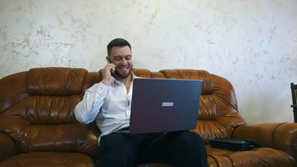 편안한 사업가는 노트북의 방에서 일하고 있습니다 무릎에 노트북을 잘생긴 전화에 — 비디오