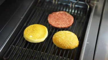İki hamburger ekmeği ve bir pirzola ızgarada pişiriliyor. Lezzetli ev yapımı hamburger..