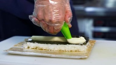 Şef suşiye krem peynir koyar. Suşi pişirme, hazırlanma süreci. Japon mutfağı konsepti. Karmaşık yemeğin süreci.