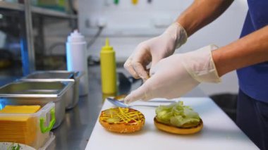 Lateks eldivenli eller kızarmış çöreğin üstüne turşu koyar. Beyaz masada hamburger yapmak. Fast food konsepti videosu.
