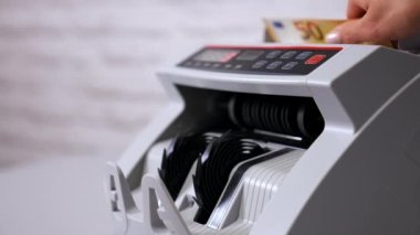 Kadın veznedar para sayma makinesine para koyuyor.