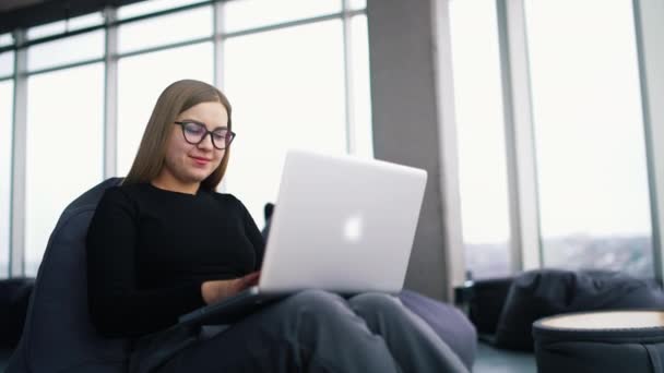 漂亮的年轻女子穿着休闲装 在室内工作时使用笔记本电脑 面带微笑 — 图库视频影像