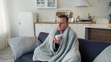 Halk tıbbı. Sıcak battaniyeye sarılıp sıcak çay içen hasta, genç bir adam. Salgın.