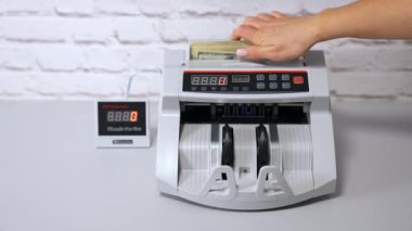 Amerikan Doları. Kadın para sayma makinesine para koyuyor..