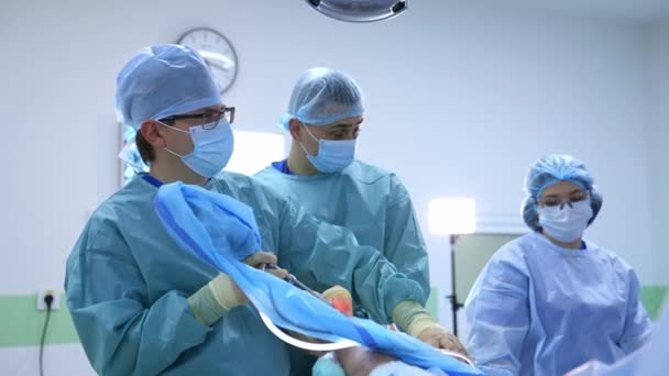 明るい現代の手術室で手術を行う外科医のチーム 手術室だ 診療所の近代的な設備 — ストック動画