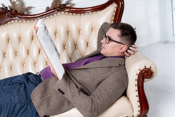 Man Relaxing on a Couch with a Book. A man laying on a couch reading a book