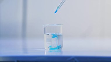 Bardak dolusu su laboratuvar masasına konur. Suya birkaç damla mavi sıvı dökülüyor. Bebek bezi incelemesi.