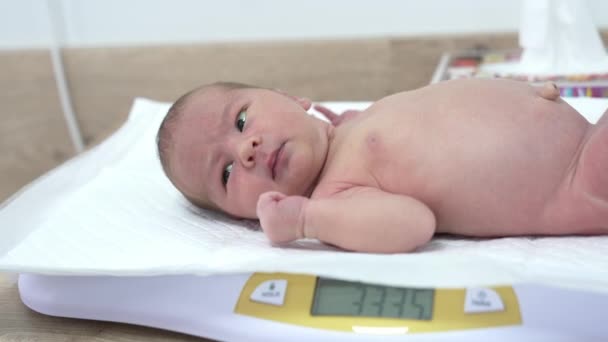 裸の子供が電子スケールとヒッカップに横たわっている かわいい新生児が病院のマタニティユニットで体重を測定されています — ストック動画