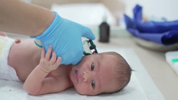 手袋の中の小児科医の手は 幼児の耳の近くに特別な装置を保管しています 病院における赤ちゃんの健康管理について — ストック動画