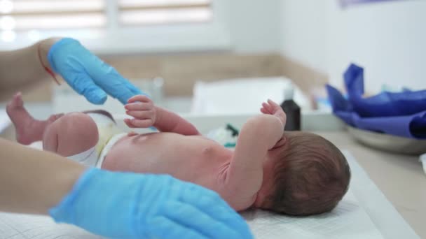 小児科医のテーブルの上に横たわっているおむつの中の小さな赤ちゃん 青い手袋のネオシノロジストの手は子供を連れて後ろ向きに回しています — ストック動画