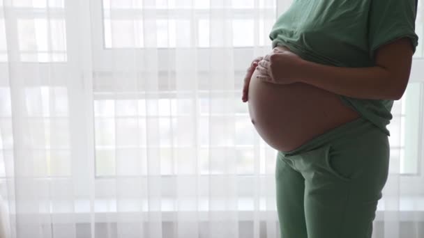 大肚子的孕妇走到大灯窗前 未来的妈妈温柔而亲切地抚摸着她的肚子 — 图库视频影像